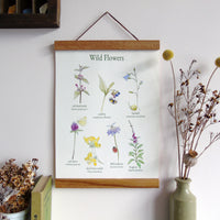 Floral illustration poster with wooden frame hanging on a wall next to a vase with dried flowers.